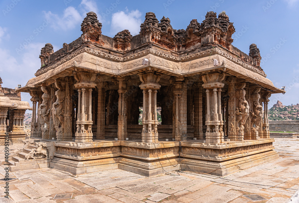 Hampi, Karnataka, India - November 5, 2013: Vijaya Vitthala Temple. Closeup of main brown stone sanctuary seen from cormer and looking through it under blue cloudscape. 