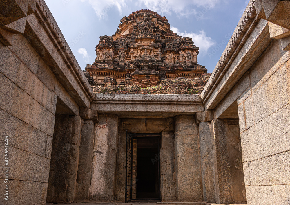 Hampi, Karnataka, India - November 5, 2013: Vijaya Vitthala Temple. Small open space in center of sanctum shows blue cloudscape and top of West is back entrance red stone Gopuram.