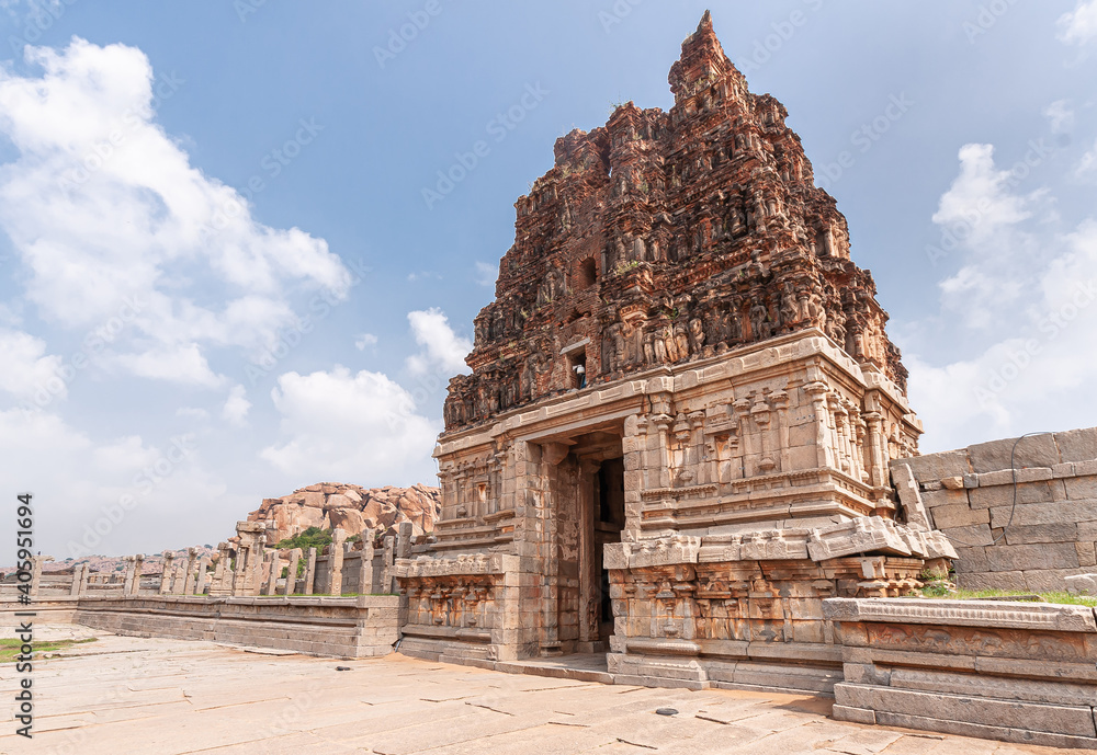 Hampi, Karnataka, India - November 5, 2013: Vijaya Vitthala Temple. Wider views on Red stone gopuram on top of beige stone east entrance gate under blue cloudscape.