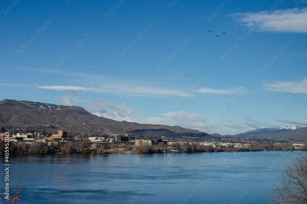 A city behind a wide river against a background of blue mountains on a sunny day against a background of a bright blue sky. Washington state, USA