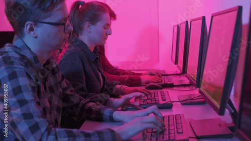Three adults work online in an office, two men and one woman. Pink bright light. Dark in the room, night. 4k video.