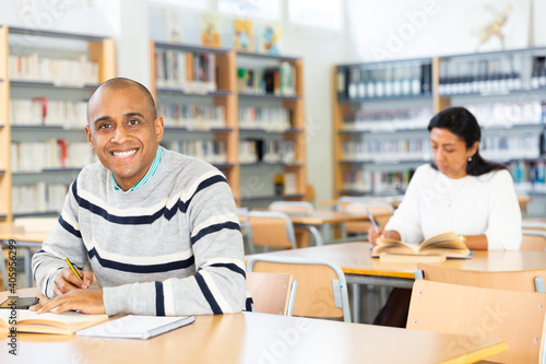 Young adult man working with books, finding information at library
