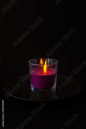 Vertical shot of a purple lit glass candle isolated on black backgrou photo