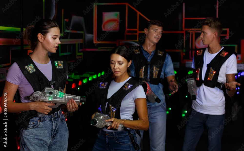 Two pretty girls talking and holding guns during laser tag game with men in dark labyrinth