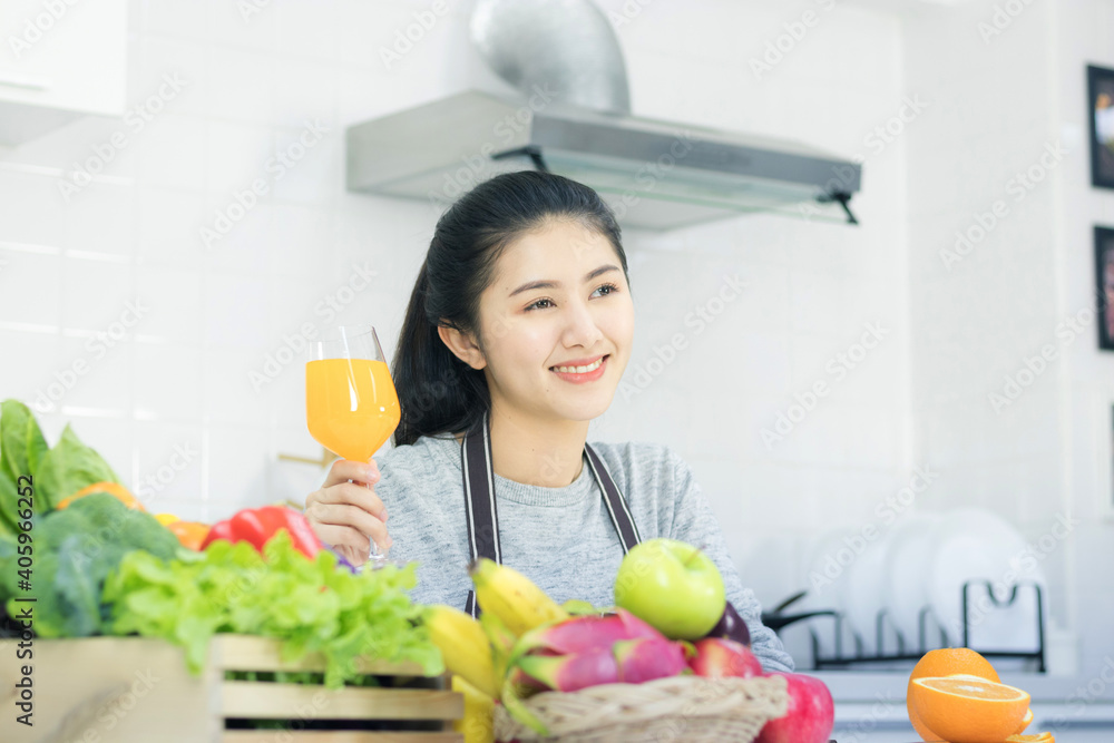 Asian women taking care of health and body shape Preparing food in the kitchen and waiting to drink orange juice in the glass.

