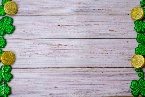 Glitter Four Leaf Clovers and Gold Coins on the edge of the frame on a White Wood Background