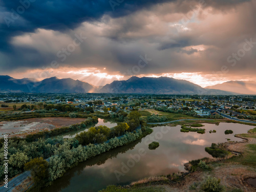 Dramatic clouds over the rugged mountains reflect off the lake by the suburban community - aerial view