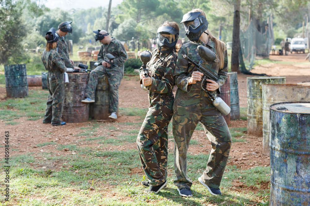 Cheerful young women friends in camouflage holding guns ready for playing paintball outdoor