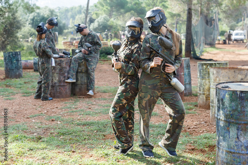Cheerful young women friends in camouflage holding guns ready for playing paintball outdoor