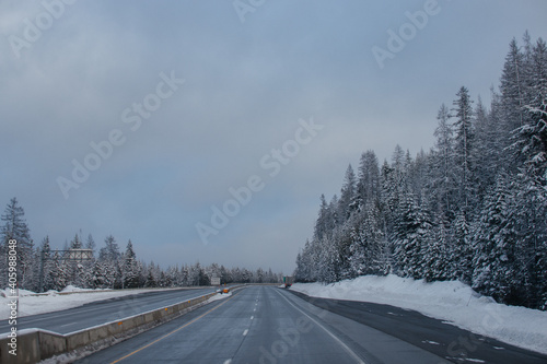 Winter highway among snow-covered mountains and tall fir trees at sunset.