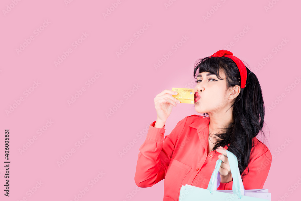 Asian woman carrying a shopping bag, she is stressed with spending credit cards, staging a studio on a pink background. Asian woman carrying a shopping bag, she is stressed with spending credit cards, staging a studio on a pink background.