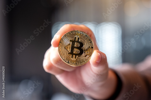 Closeup image of a hand holding and showing a golden color bitcoin