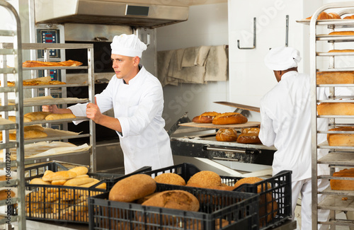 Portrait of confident male chef pushing rack trolley with fresh bread in bakery kitchen