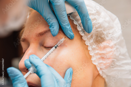 Adult woman with wrinkles around her eyes in process rejuvenation injections of hyaluronic acid filler, close up. Cosmetologist injects botulinum toxin to smooth female face skin.