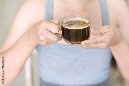 Closeup woman hand holding glass of hot americano coffee, selective focus, vintage tone