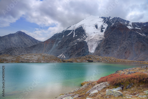 Mountain landscape. High mountain and green lake. Selective focus on the snowy mountain peak. © Sergei