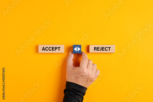 Male hand holds a wooden cube with arrow icon between the options of accept or reject. photo