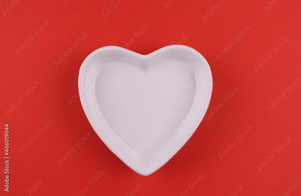 White ceramic plate in the shape of a heart on a red background. Valentine's day photography White ceramic plate in the shape of a heart on a red background. Valentine's day photography