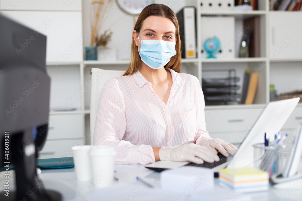 Female office worker in protective medical mask is having productive day at work in office