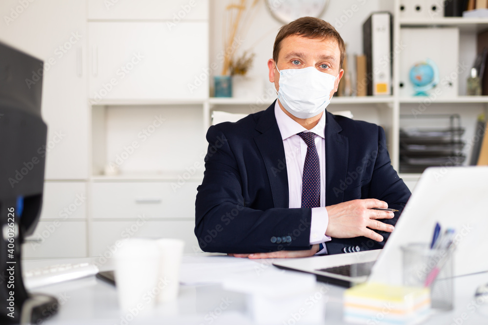 Focused businessman in disposable face mask working on laptop in office. Necessary precautions during COVID 19 pandemic