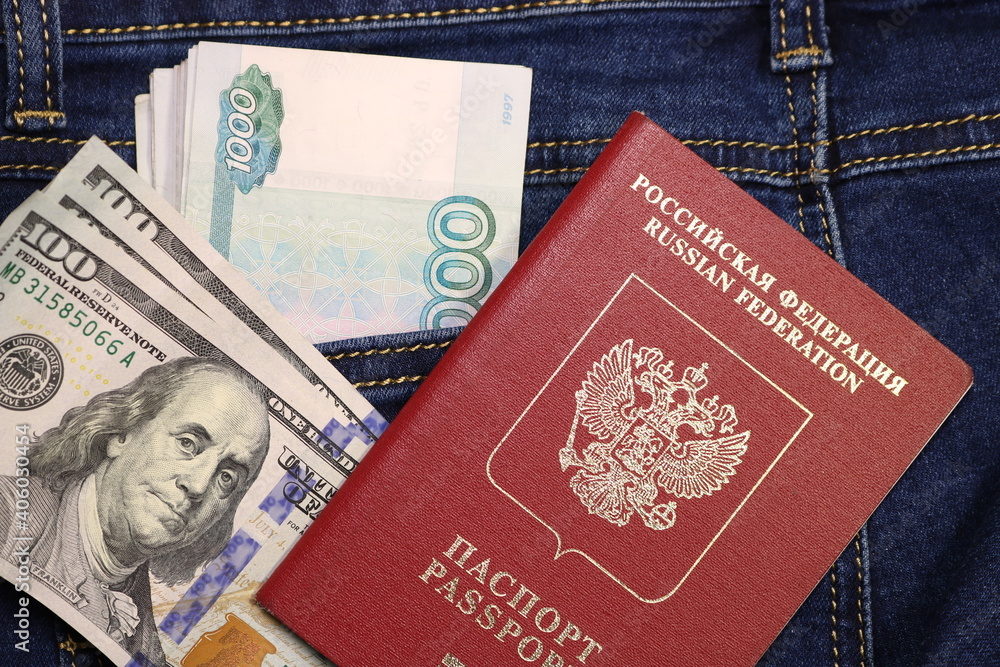 A pack of American hundred dollar bills and Russian rubles in a pocket of blue jeans and an international passport of Russia. Money in your pocket, cash. Travel concept. A pack of American hundred dollar bills and Russian rubles in a pocket of blue jeans and an international passport of Russia. Money in your pocket, cash. Travel concept.