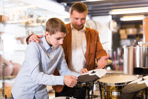 positive american teenager and father deciding on drum unit in musical shop