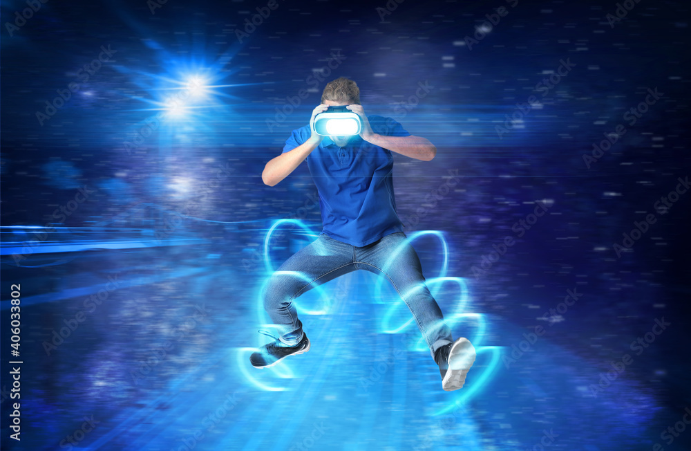 Young man with VR glasses playing video games on dark color background