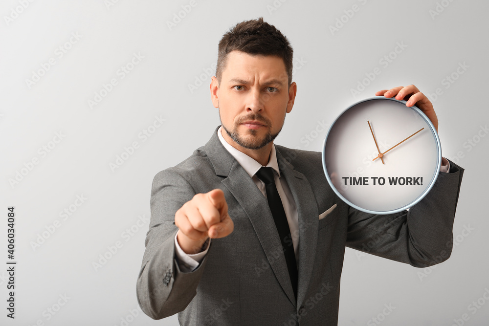 Businessman holding clock with text TIME TO WORK on light background Businessman holding clock with text TIME TO WORK on light background