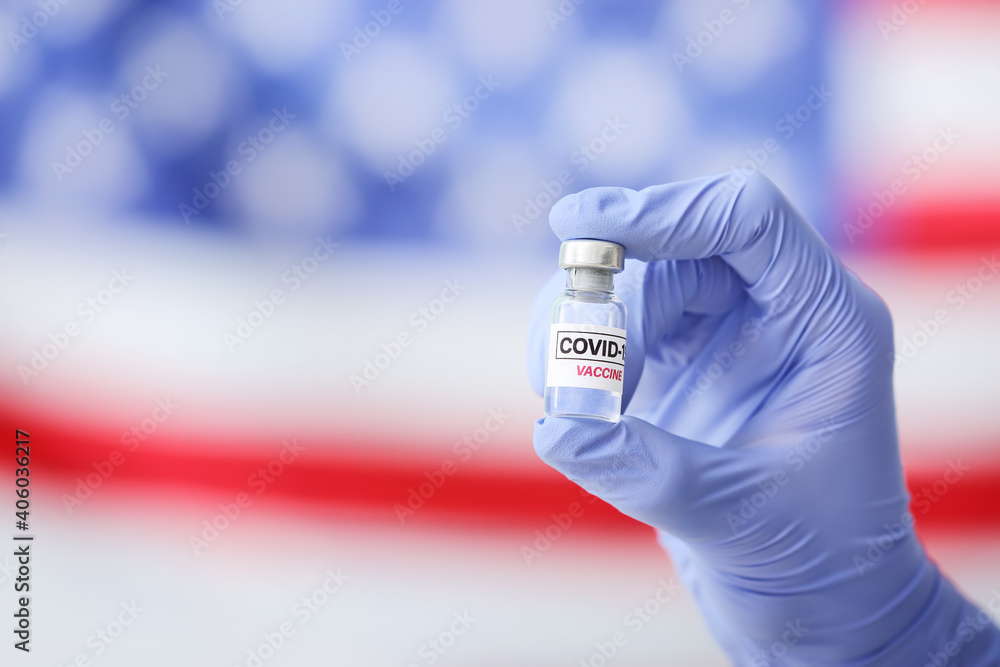 Doctor's hand with COVID-19 vaccine against USA flag