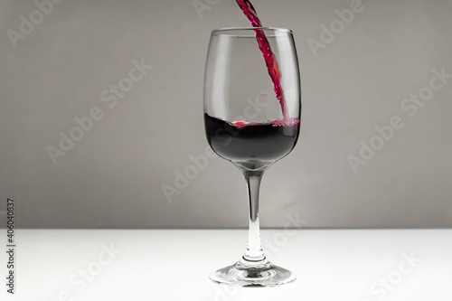 Red wine is poured from a bottle into a glass on a blurred background, close-up. Horizontal photo