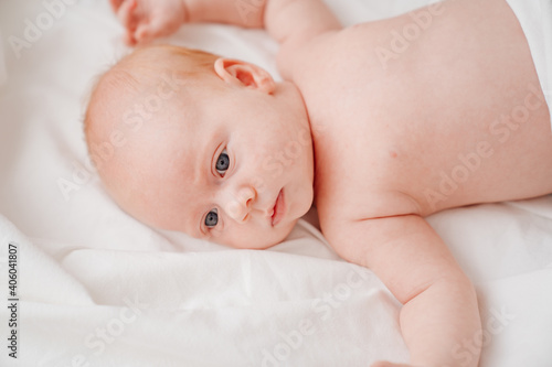 cute red-haired baby lies on a white bed. concept of baby care