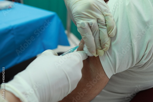 a close up photo of an intra muscular covid vaccine being given in arm of a patient by a doctor with gloved hand with selective focus on arm