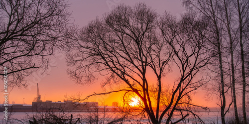 Sunrise over the city in winter. The frozen river and bare trees.