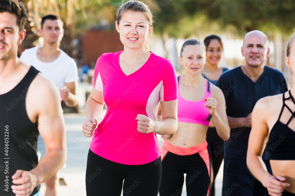 Sporty women and men running along embankment in sunny morning