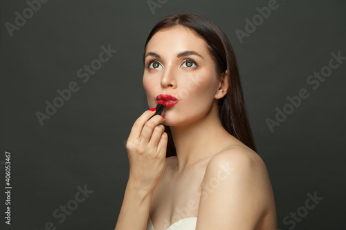 Young woman applying red lipstick makeup on lips on black background