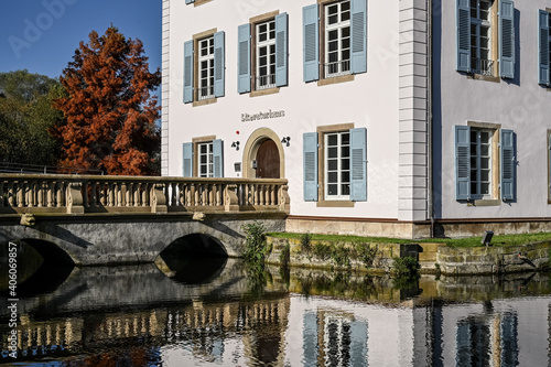 A baroque house, called Trappenseeschlösschen, surrounded by Lake Trappensee in Heilbronn, Germany during autumn. A pedestrian bridge leads to the house. photo