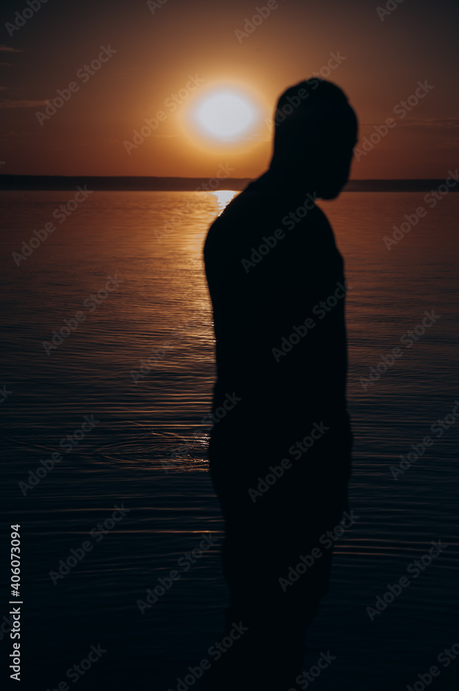 a man looks at the lake against the background of the sunset