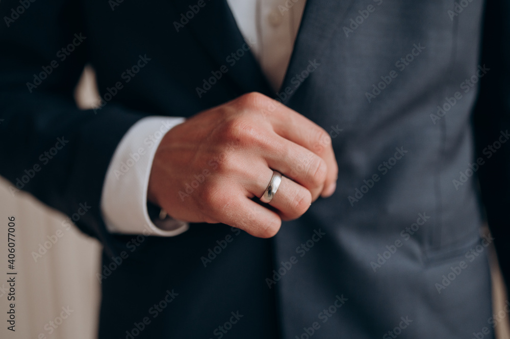 the groom in a black jacket and white shirt with a ring on his hand holds a jacket