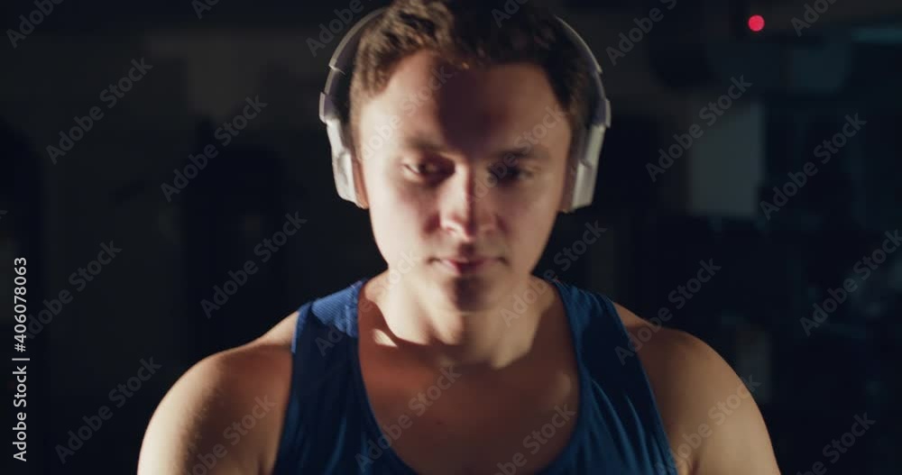 Portrait of athlete with headphones, walking fast on a treadmill in a dark gym Portrait of athlete with headphones, walking fast on a treadmill in a dark gym