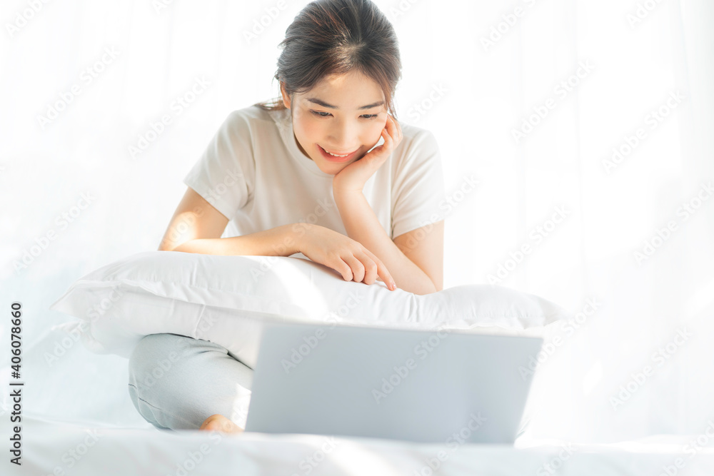 Young Asian woman sitting on bed working watching home entertainment Young Asian woman sitting on bed working watching home entertainment
