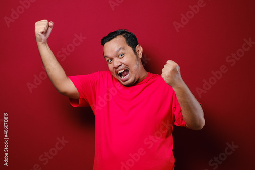 Young asian man happy and excited expressing winning gesture. Successful and celebrating over red background