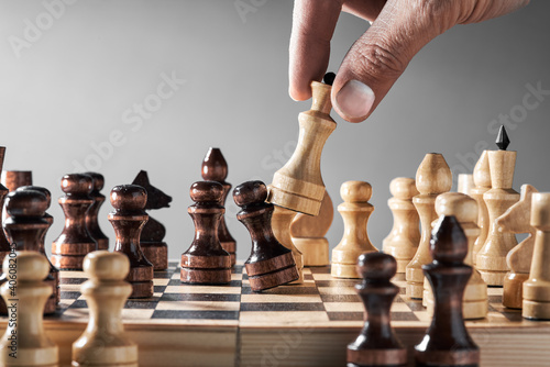 Wooden chess pieces on a chessboard, a hand with a white queen makes a move, the concept of strategy, planning and decision making. The concept of leadership and teamwork to achieve success.