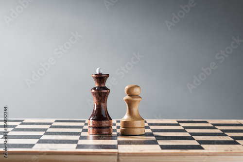 Wooden chess pieces on a chessboard, the confrontation of the white pawn and the black queen, planning and decision-making concept. The concept of leadership and teamwork to achieve success.