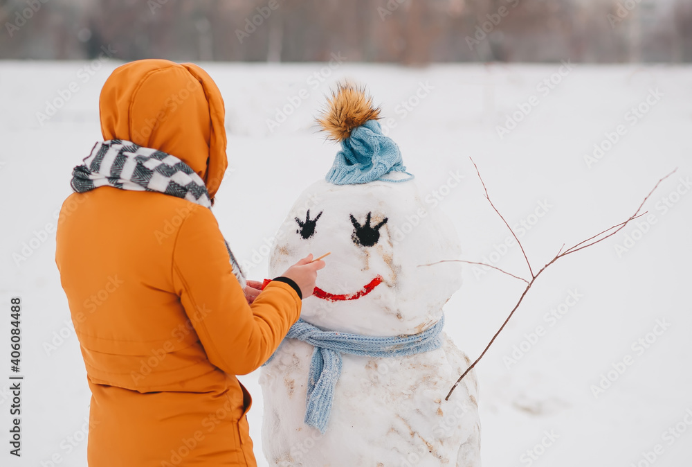 Young woman making a snowman in a park in winter.