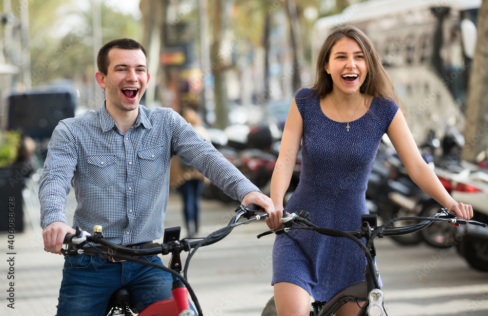 Obraz premium Cheerful young couple riding on electric bikes outside and laughing. Selective focus.