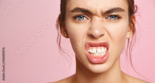 Sassy young woman showing white teeth, showing confident face, fighting blemishes and acne with facial cleansing gels and toners with deep hydration and nourish effect, pink background