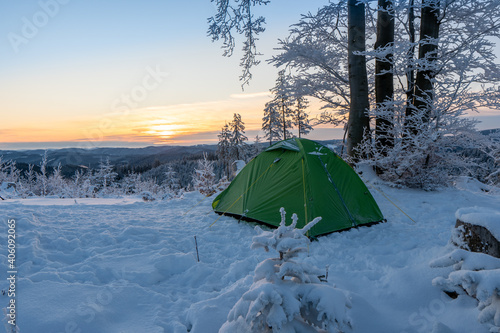 Amazing landscape on the cold winter day. Sunset. On the lawn green touristic tent stands with wide path to it. Beautiful snowy forest with pine trees in mountains. Wallpaper background.