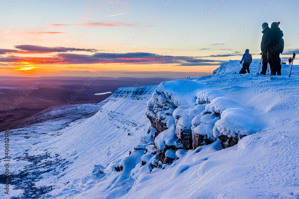 Hikers watching sunrise on top of a snow-covered mountain