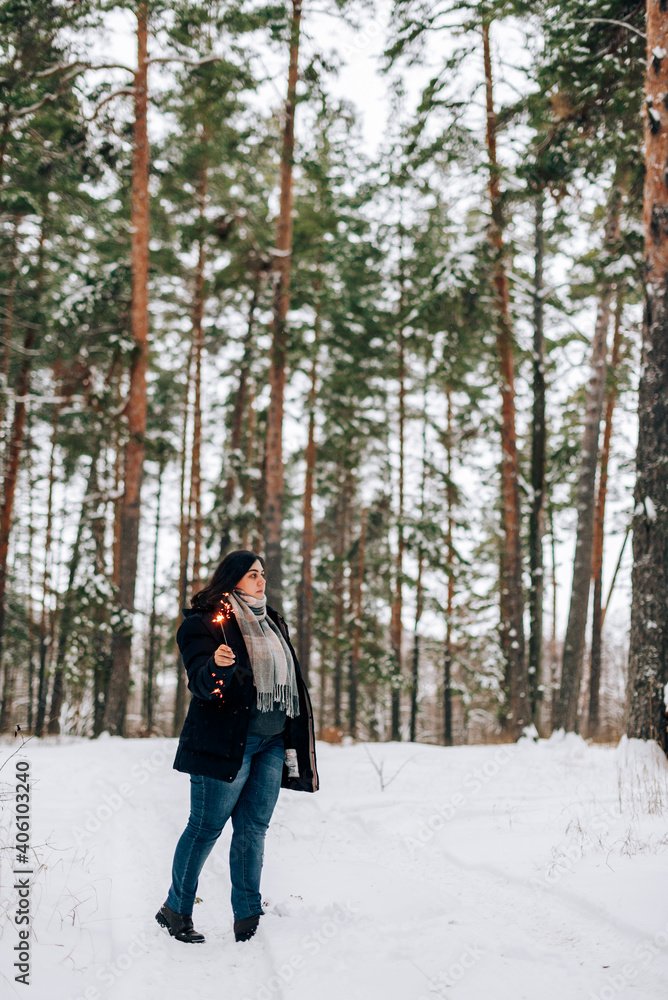 Adult young woman with sparklers on the background of winter pine forest