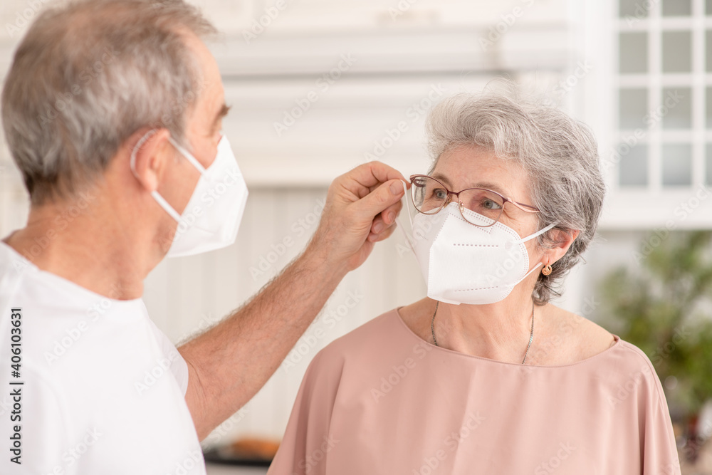 Senior man putting on surgical mask on his elderly wife ill woman during the coronavirus epidemic